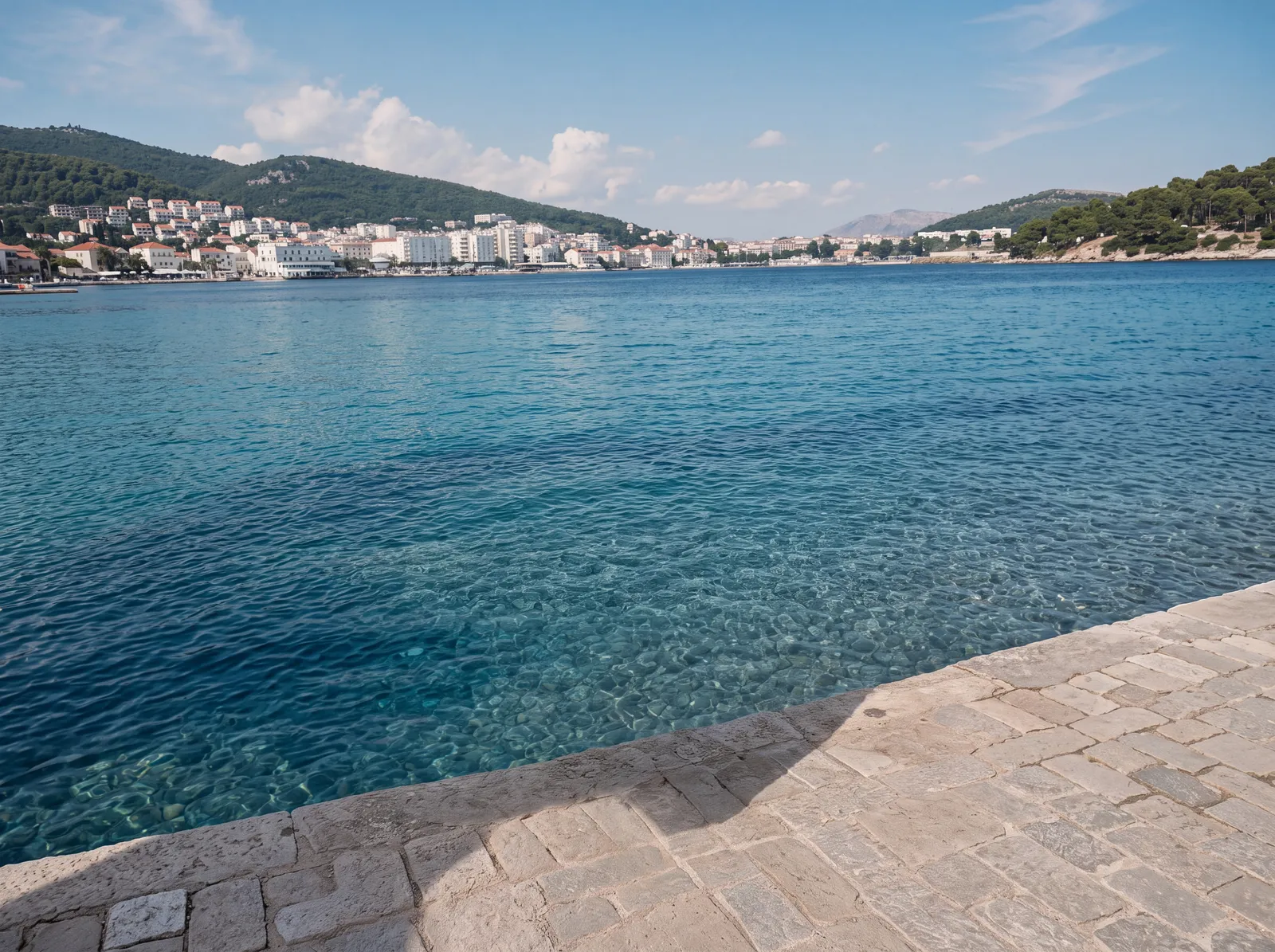 Turquoise harbour water and a stone promenade with a coastal town behind
